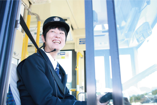 バスの運転席の車窓から外に笑顔を向ける辰巳運転士